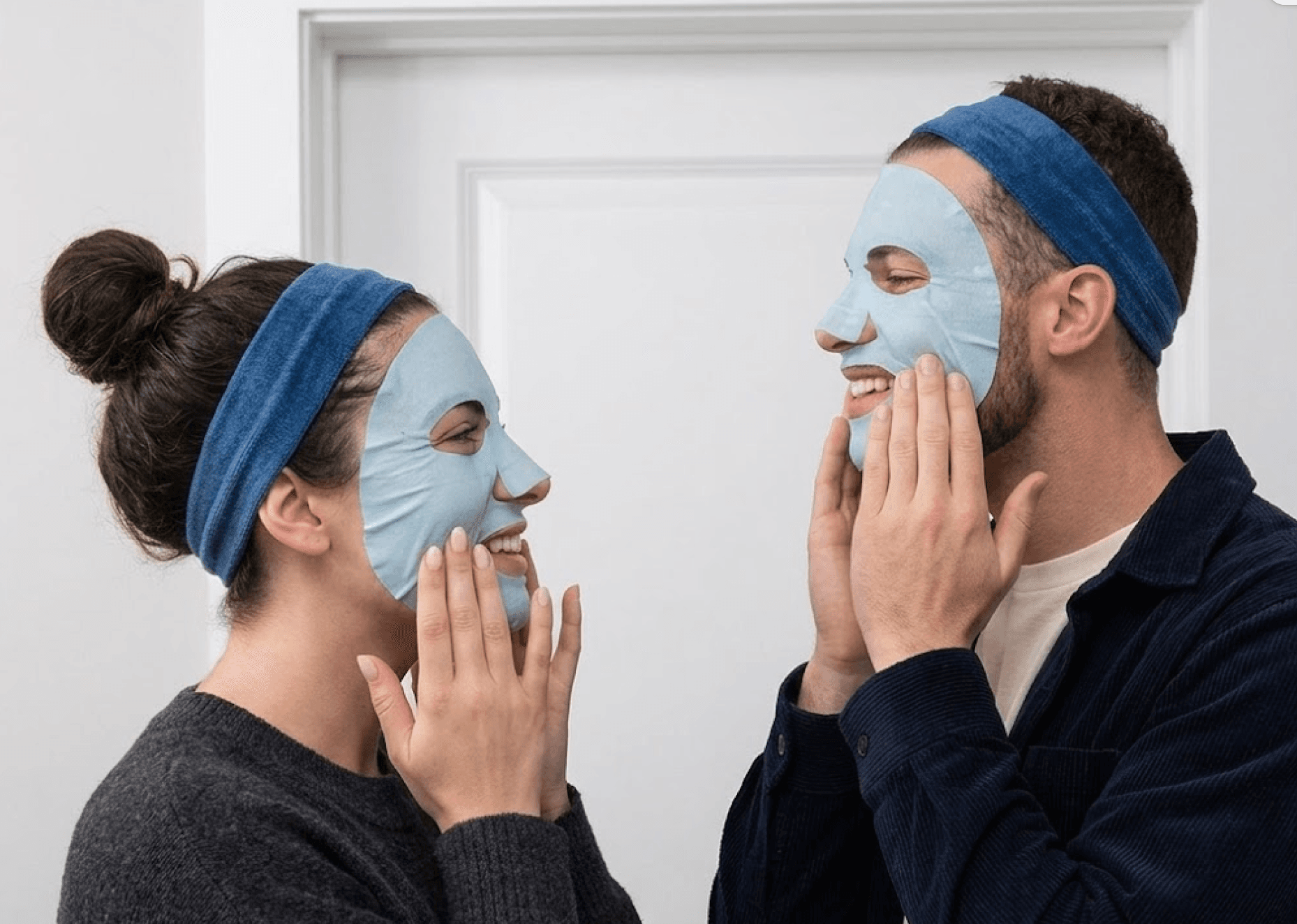 Paar lacht, während es zu Hause Sheet Masks aufträgt